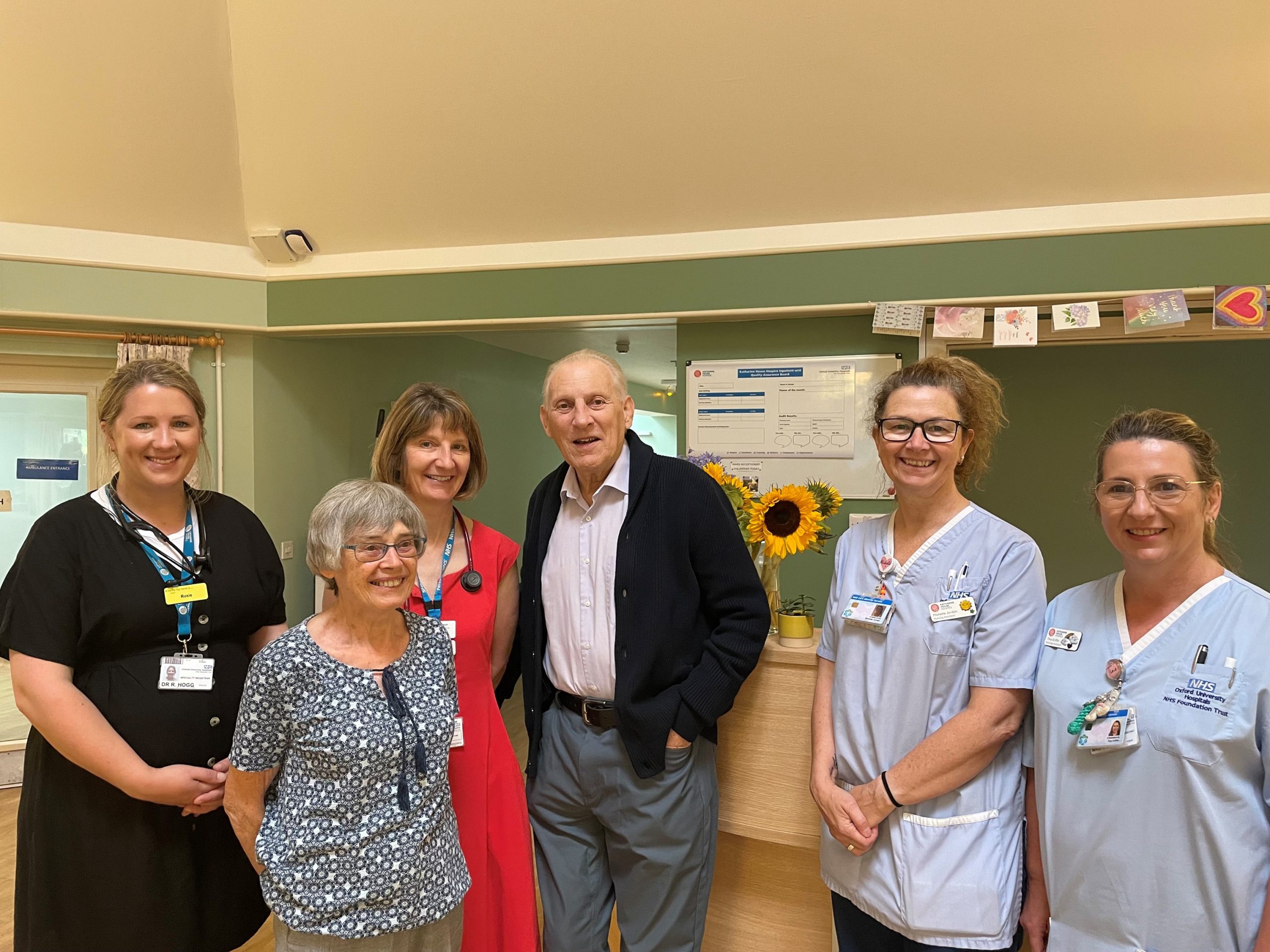 A group of six people, including healthcare workers, smiling and standing in a hospital or clinic setting.