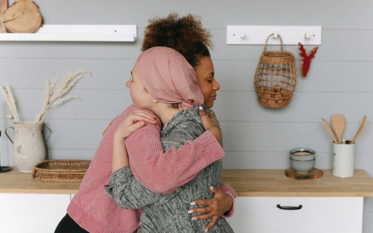 Two women hugging in a cozy kitchen setting.