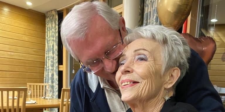 An elderly couple smiling and embracing indoors.