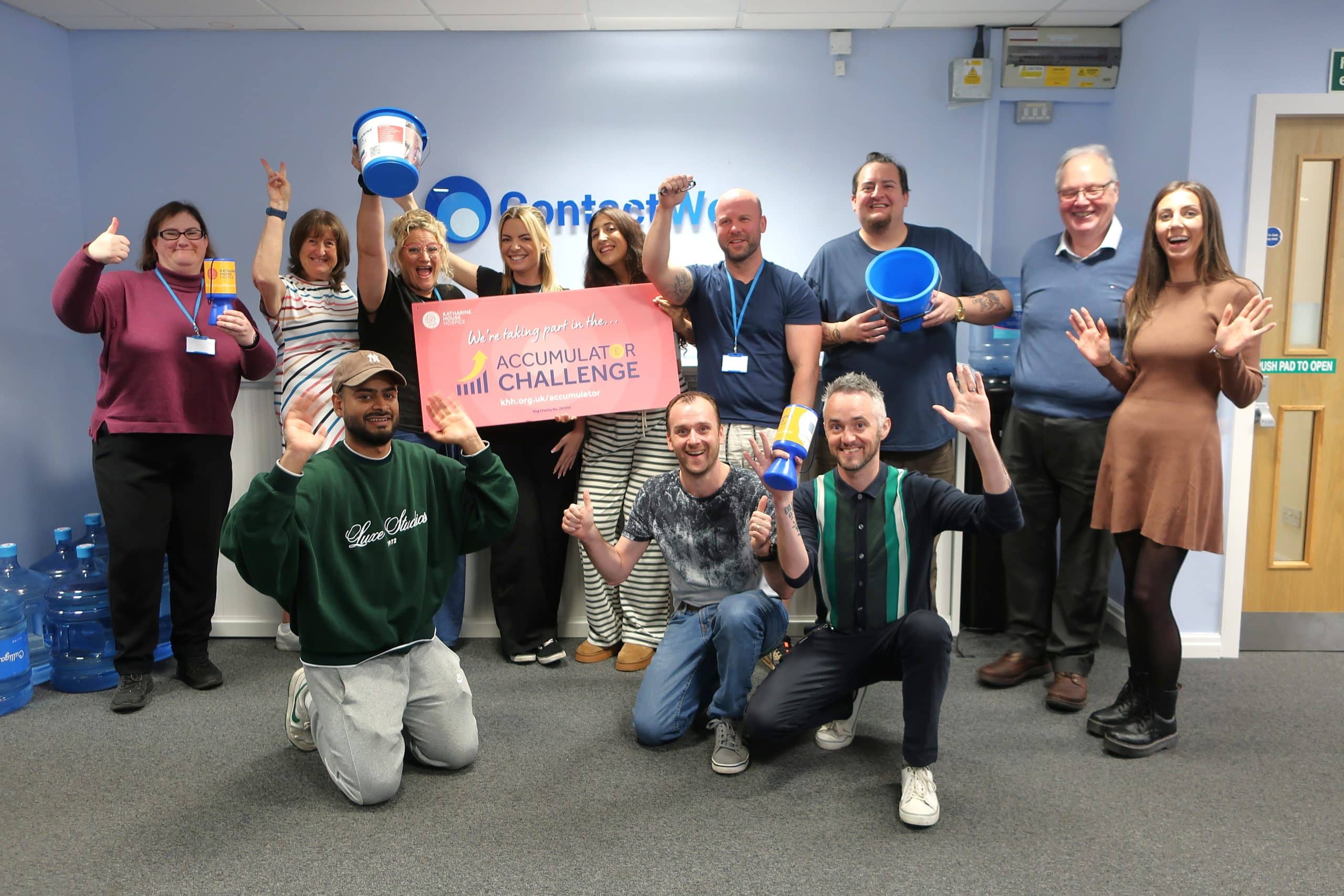 Group of people smiling and holding a sign that reads "Accumulator Challenge" in an office.
