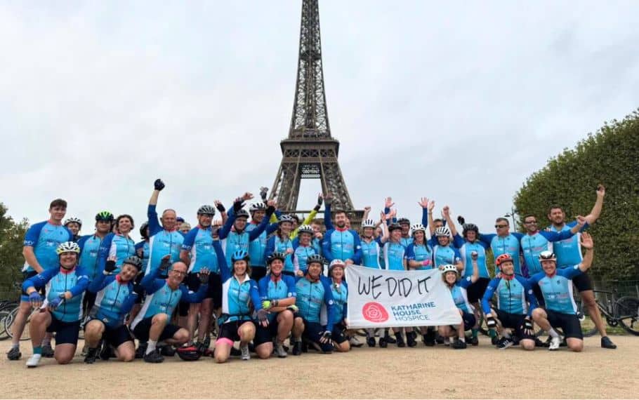 Group of cyclists celebrating with a “We Did It” banner in front of the Eiffel Tower.