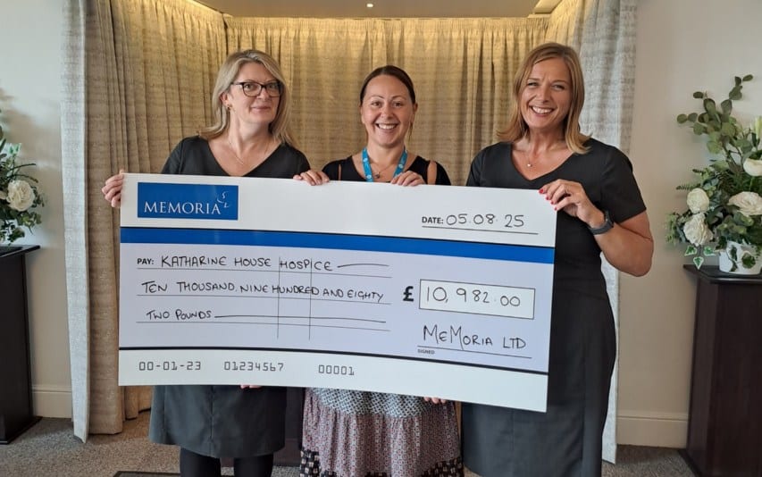 Three women holding a large charity cheque for £10,771.00 from Memoria Ltd.