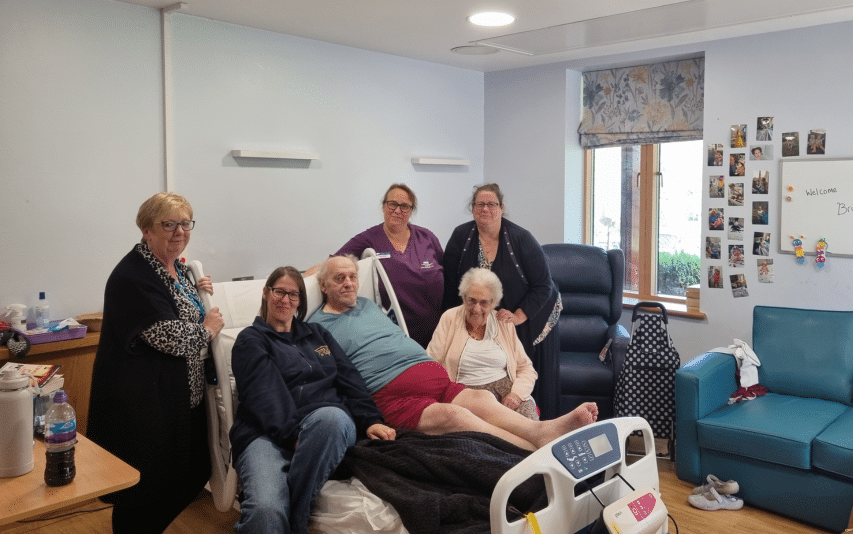 A group of people gathered around a patient in a hospital room, smiling for the photo.