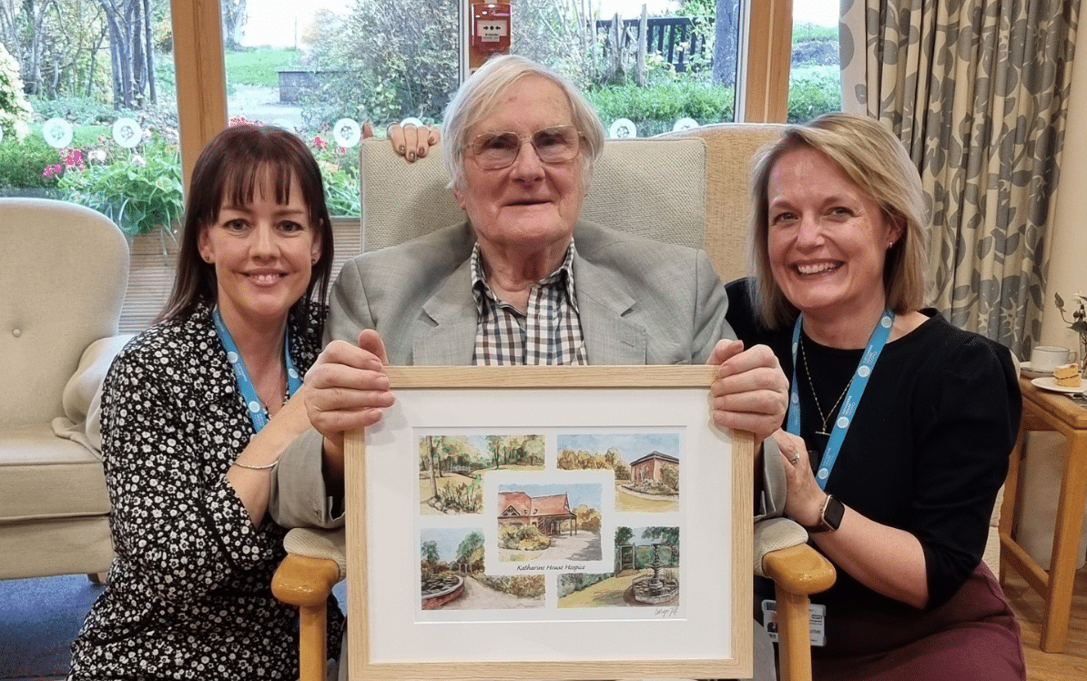 Three people smiling and holding a framed picture while sitting indoors.